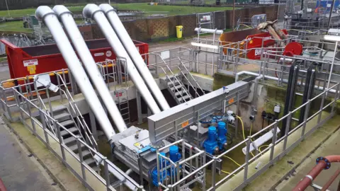 Anglian Water Steel equipment can be seen at a sewage works in Whitlingham, Norfolk, with skips underneath large pipes to collect waste