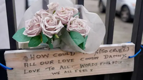 Linsey Smith/BBC A sign and a bunch of fake flowers attached to the black railings around the former Legacy premises.
