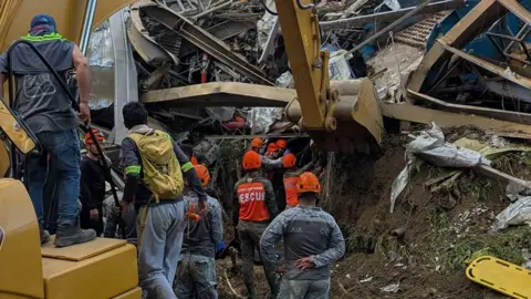 Facebook/Nestor Archival Backview of rescuers with orange helmets looking at a collapsed section of the landfill