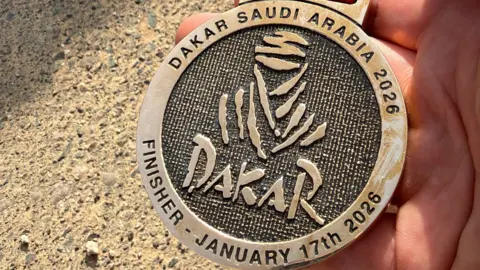 Robbie Wallace A Dakar Rally finisher's medal for 2026 being held in a man's hand