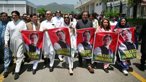 Getty Images Parlementsleden van Pakistan Tehreek-e-Insaf (PTI) dragen posters van de gevangengenomen voormalige premier Imran Khan, tijdens een protest buiten het parlementsgebouw in Islamabad op 18 juli 2024.