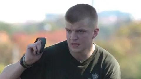 BBC L/Cpl Spencer has a look of determination on his face as he carries out a training exercise. He is wearing a green T-shirt with the Rifles' badge.