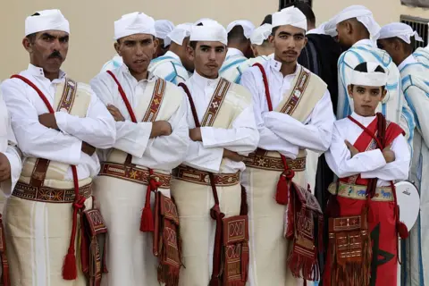 ABDEL MAJID BZIOUAT / AFP / GETTY IMAGES Men and boys dressed in white and red Amazigh clothing stand in a row.