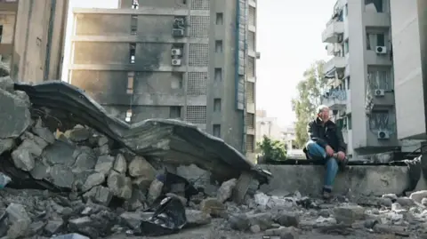 A man sits in rubble in corniche al mazraa