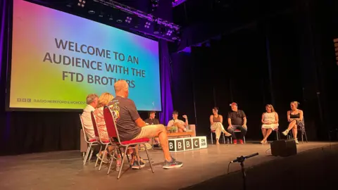 Several people are on stage with a multicoloured screen that reads: "Welcome to and audience with the FTD Brothers." 