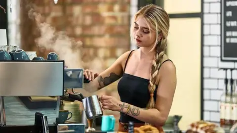 Getty Images A young female worker uses a coffee machine in a shop.