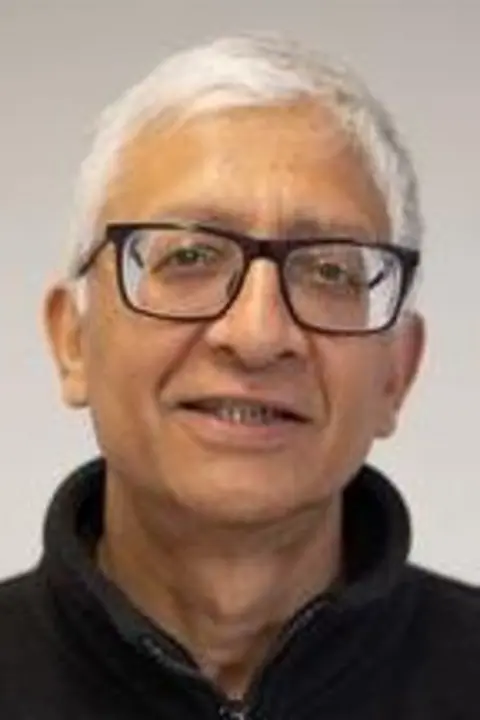 A representation    photograph   of Dr Ravi Kumar who is wearing a achromatic  zip-up fleece and glasses