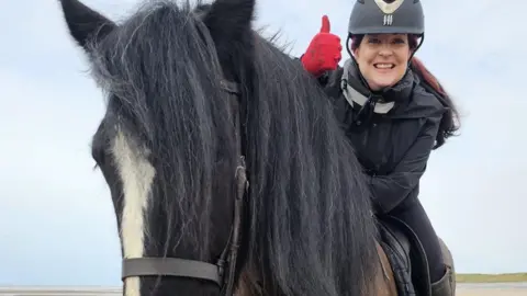 Cumbria Heavy Horses Harriet Martin and Guinness. They are facing the camera and Martin is smiling with her teeth and holding her thumb up.