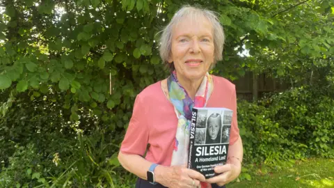 Dagmar Smeed Ute Smeed, an elderly lady with grey hair. She is wearing a pink top, and has a scarf on, and is holding her book
