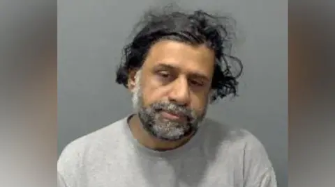 Mohammed Hamid tilts his head and looks to the camera wearing what looks to be a prison issue grey sweatshirt. 