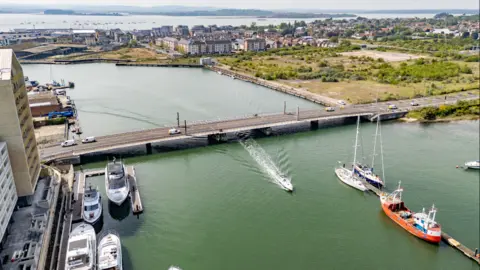 The Twin Sails Bridge connects Poole with Hamworthy - the bridge goes over a river and the image shows several boats not far from the bridge.
