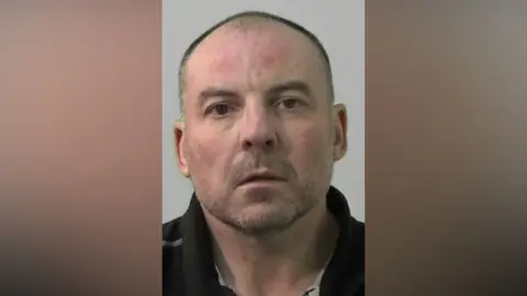 Mugshot of William Gardner. He has a shaved head and very short stubbly beard.