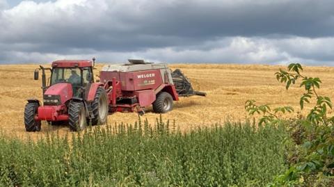 A red tractor is pulling a harvesting machine under heavy cloud