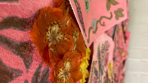 A close-up of orange pressed flowers attached to pink cloth with blue and green patterns drawn on it
