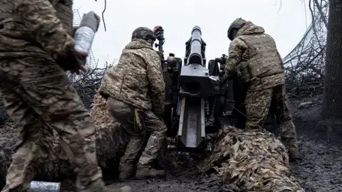 Ukrainian soldiers preparing to fire a howitzer in the Kharkiv region - three men wearing camouflage load the gun