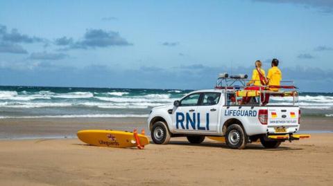 Two lifeguards sitting on a lifeguard truck watching the waves at Fistral Beach