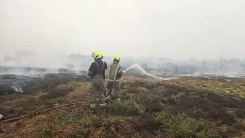 Suffolk County Council Two firefighters with hoses are spraying water on to burning heathland.