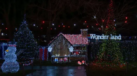 Melksham News A grotto display in Sarum Avenue, Melksham, Wiltshire. Two large Christmas trees are planted either side of the grotto and there are large presents and a snowman light. The word "Wonderland" is also spelled out in lights. 