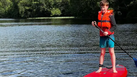 NHSGGC A young boy stadning on a paddleboard wearing a red lifejacket
