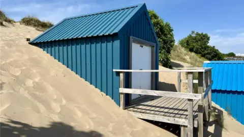 Beresford Adams Beach hut partly covered in sand