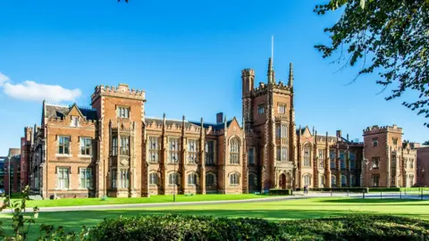 Getty Images The outside of Queen's University Belfast. There is a large area of grass in front of the building and a blue sky above. 