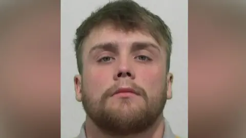 Mugshot of Kennedy. He has a short thick fair beard and short thick fair hair