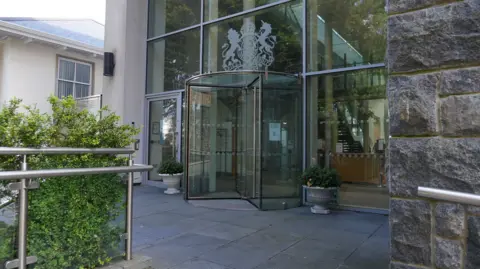 Guernsey's Royal Court - A building with a glass revolving door, amnd the crest of the Royal Court on it. A lion and a horse either side of a circle with a crown on top. 