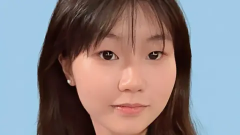 Close-up of a young Chinese girl smiling at the camera, against a blue background