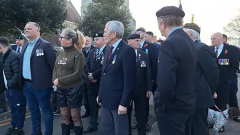 BBC/Stuart Maisner A group of people gather wearing military uniforms. 