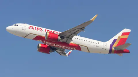 An Air India plane - white with red lettering and a red, gold and purple pattern at the tail - flying against a blue sky 