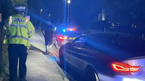 Police officers by two stopped cars on the road. It is nighttime. 