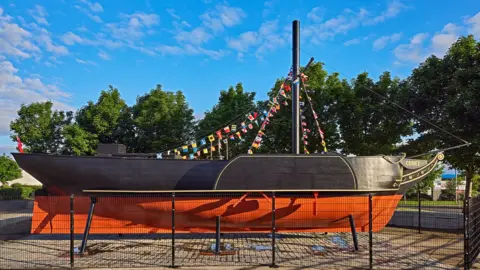 A side-on view of Comet, black above the waterline, red below it with a funnel decked with bunting