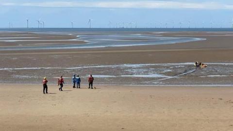 Wirral Coastguard Rescue Team on beach rescuing woman from sand