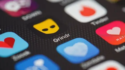 Getty Images The Grindr app on a phone alongside blurred out other apps. Grindr is black with an orange mask.