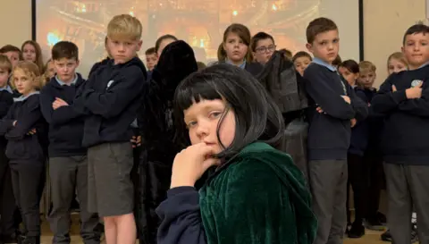 A child dressed up as Claudia Winkleman surrounded by other pupils