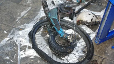 An image of a fire-damaged bike laying on a concrete floor