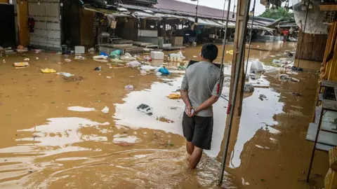 Getty Images A man watches, back facing the camera, as muddy floodwaters rise in city of Hoi An 