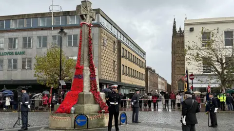 Military veterans and personnel are gathered at the Burma War Memorial in Taunton which is covered in a blanket of poppies. 