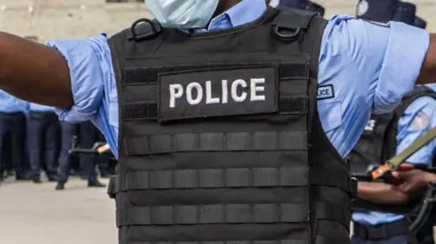 A police officer wearing a short-sleeved blue shirt and black flack jacket emblazoned with the word "police".