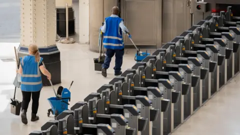 Station cleaners dressed in blue with bop buckets and deserted barriers on Waterloo station's empty main concours