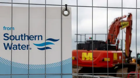 A sign reading Southern Water with a digger in the background. 