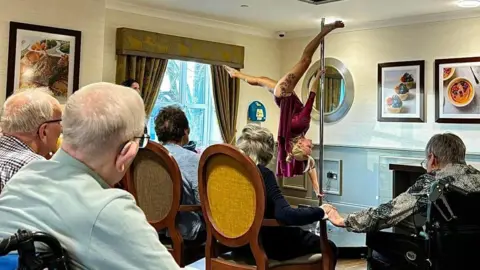 Parkfield Grange Elderly people in a care home watching a pole dance demonstration. A woman is upside down on a pole while residents watch on