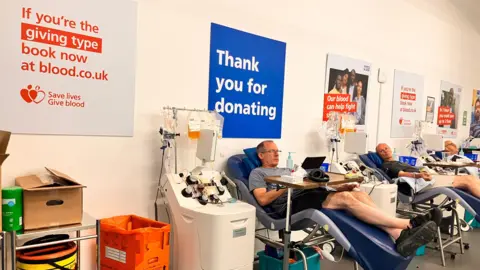 Three people on hospital chairs donating blood.