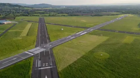 Gloucestershire Airport Limited A drone shot of the runways at Gloucestershire Airport. In the background you can see green fields.