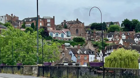 A view from behind black metal railings of many houses on the side of a hill with some larger buildings at the top