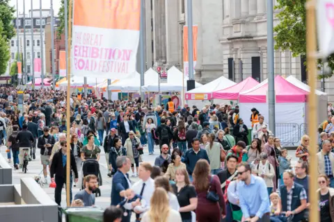 Great Exhibition Road Festival Street scene showing crowds of people walking among stalls on Great Exhibition Road. Flags with The Great Exhibition Road Festival written on them are along the street
