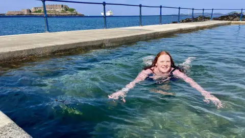 Alice swims in a sea pool along the Guernsey coast. She is looking directly at the camera and is smiling.