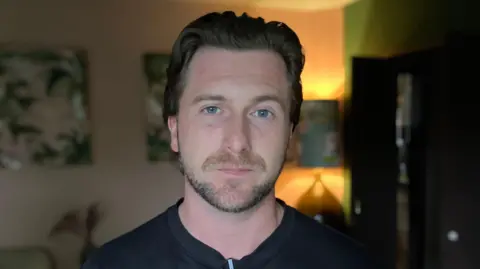 James Whitehurst has a beard and is wearing a black t-shirt.