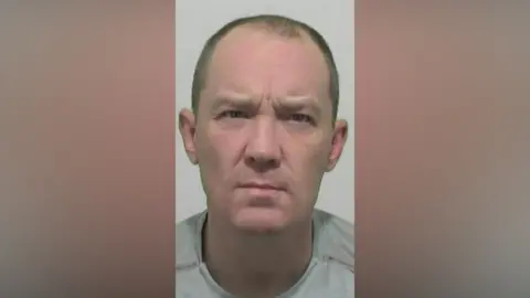 Mugshot of Thompson. He is clean shaven with short cropped fair hair.