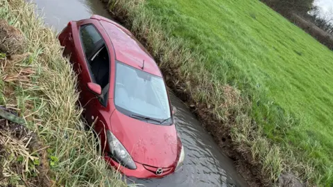 Gwent Recovery Towing Service A red car submerged in water inside a reen.
